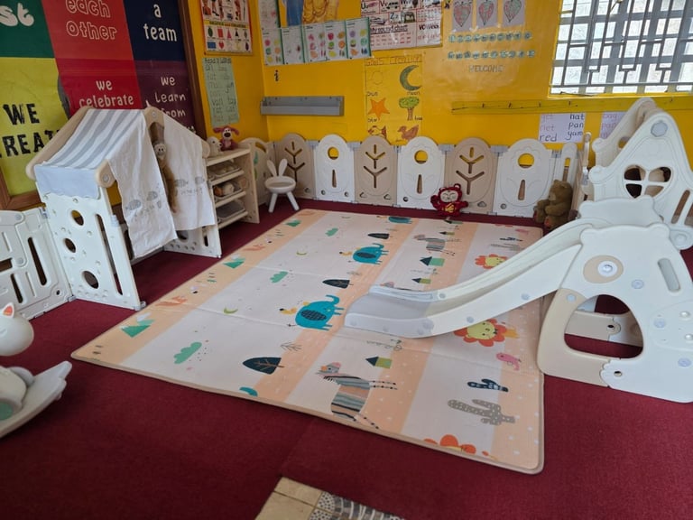 Montessori classroom with white play structures, colorful floor mat with educational activities, and yellow wall with learning posters